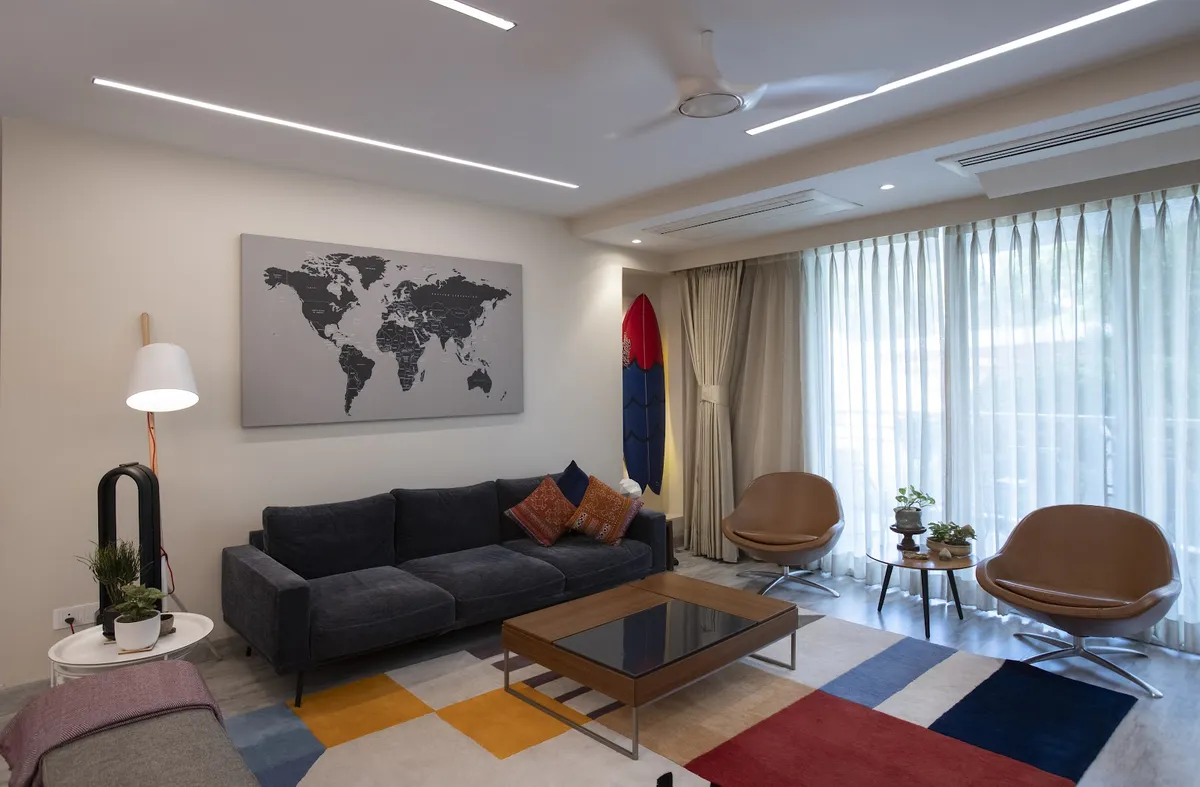 Living room with a charcoal three-seater under a grey world-map canvas, two tan swivel lounge chairs against the sheer-curtained window wall