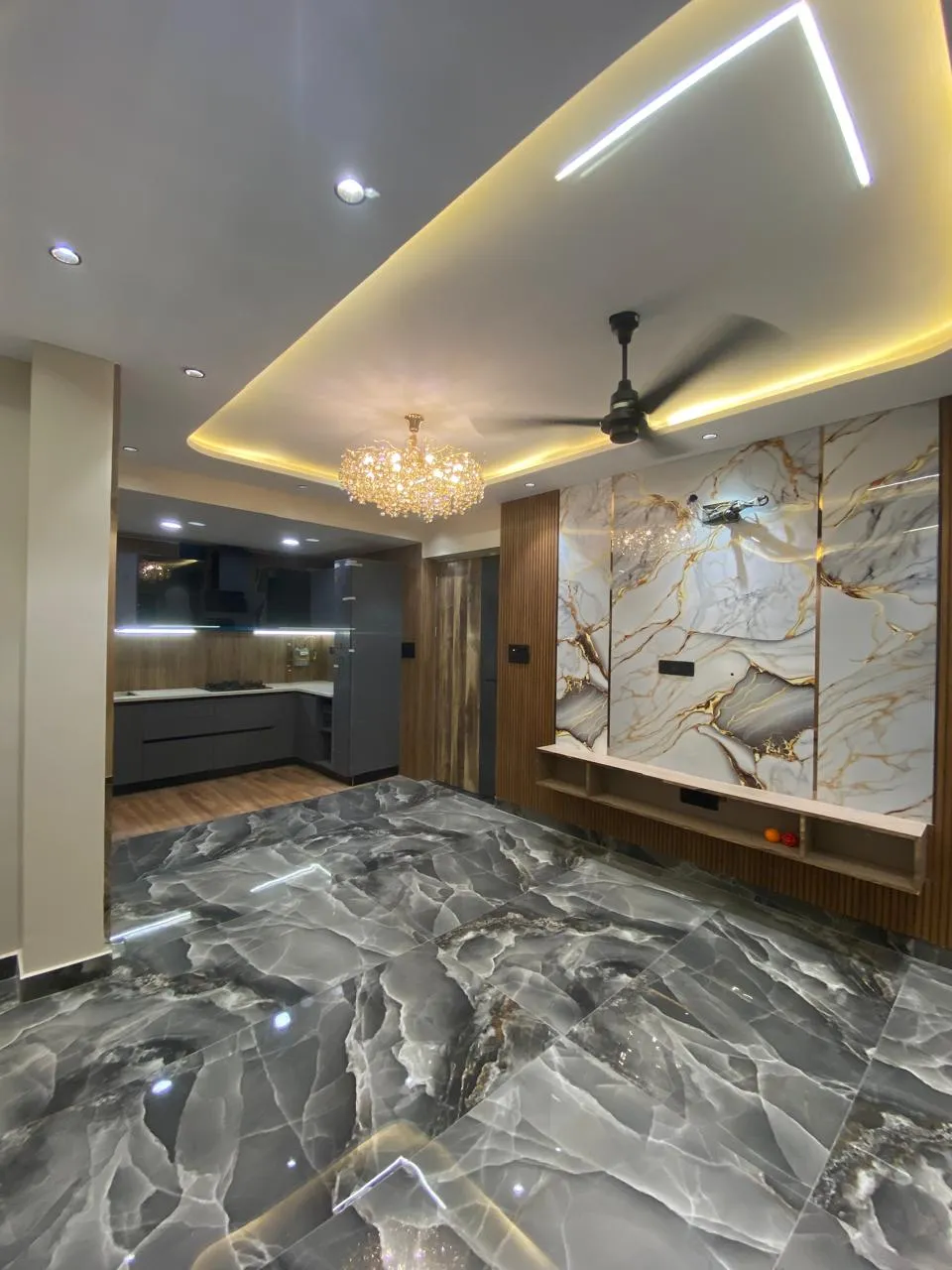 Entrance foyer with bold grey-and-gold veined marble flooring, a matching marble feature wall with cove lighting, and a crystal chandelier