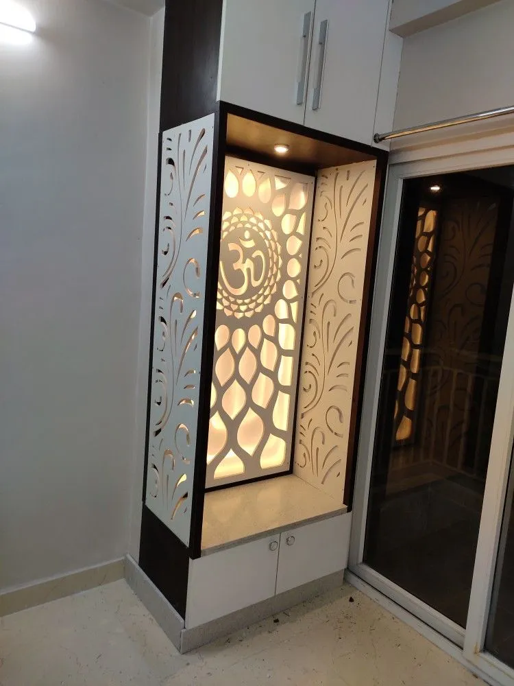 Backlit CNC-cut jaali pooja unit with an Om medallion over a lotus-petal pattern, set in a white niche with a stone platform