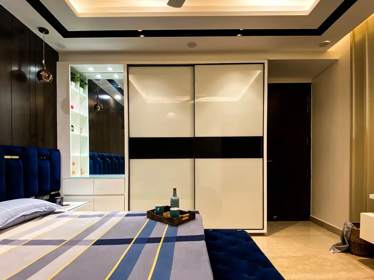 Bedroom with a royal-blue velvet channel headboard against dark veneer panelling, a white lacquered-glass sliding wardrobe banded in black