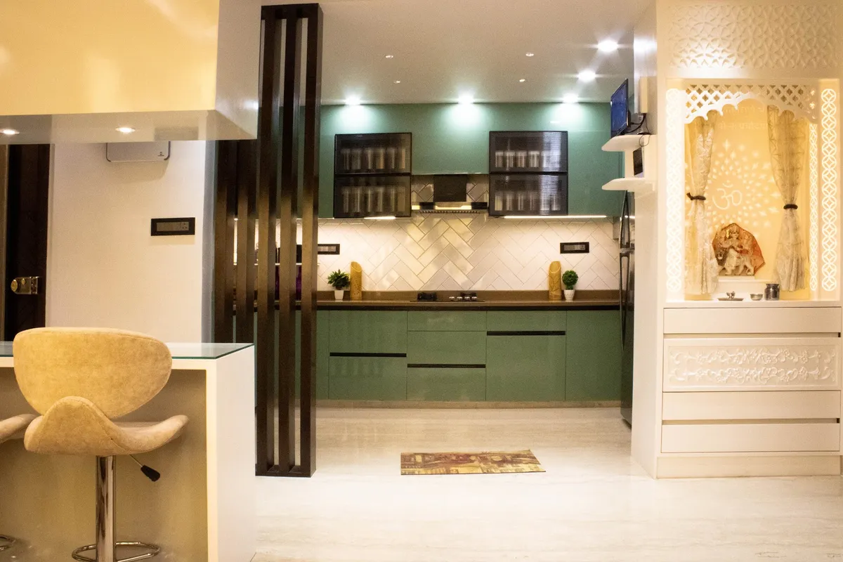 Sage-green straight-run modular kitchen with white herringbone dado, framed by a dark fluted timber partition on the left and a white CNC-jaali pooja unit on