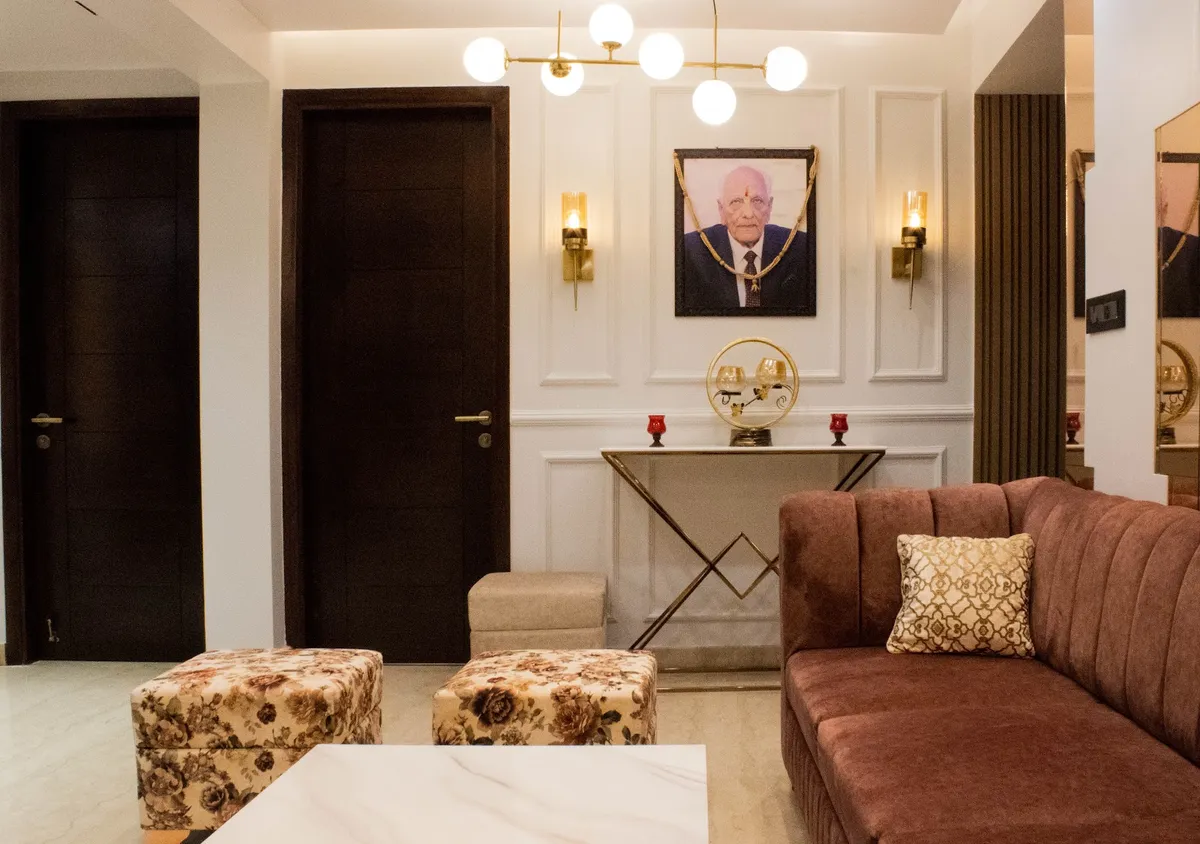 Living room entry with white wainscot panel moulding, brass wall sconces flanking a framed portrait, a gold X-base console table