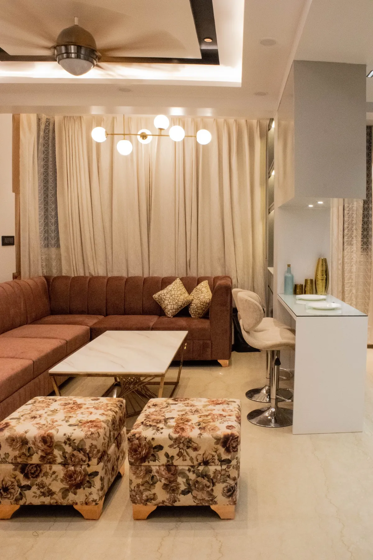 A rust-toned channel-tufted sectional sofa with floral ottomans and a marble-and-gold coffee table, beneath a brass sputnik pendant light