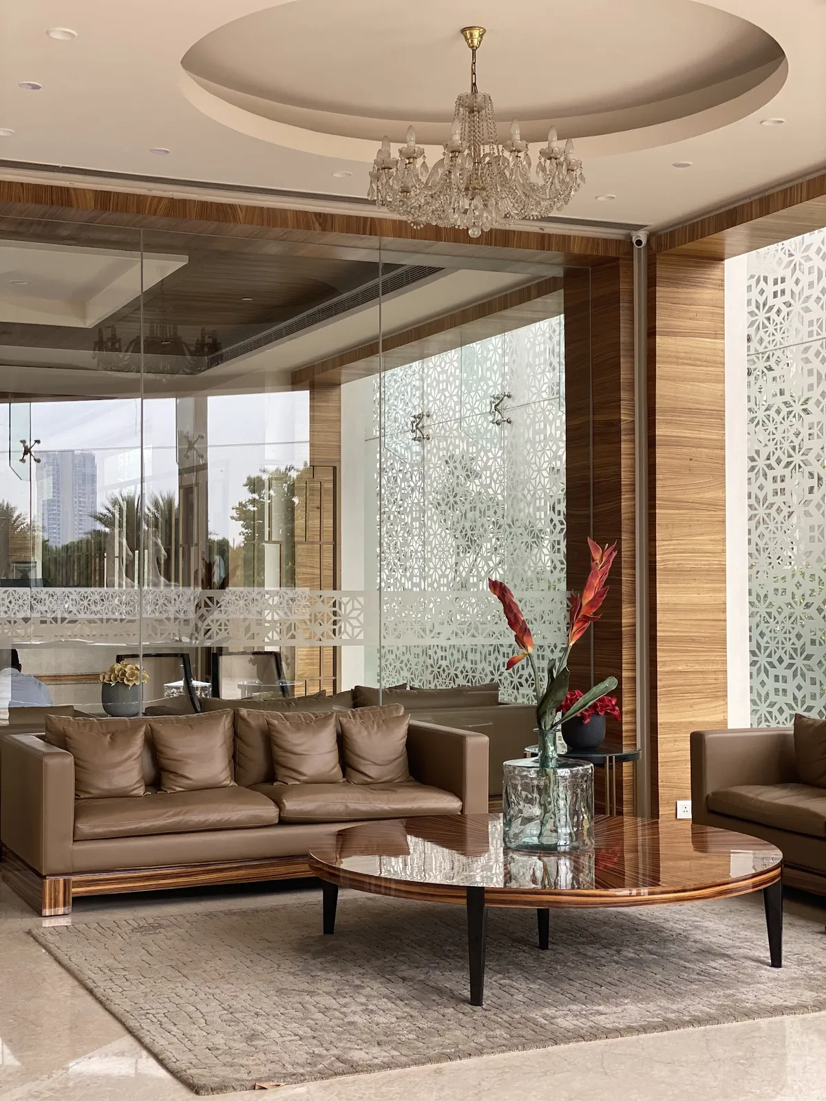 Living room with a round high-gloss wood coffee table, tan leather sofas, a crystal chandelier in a circular pop ceiling