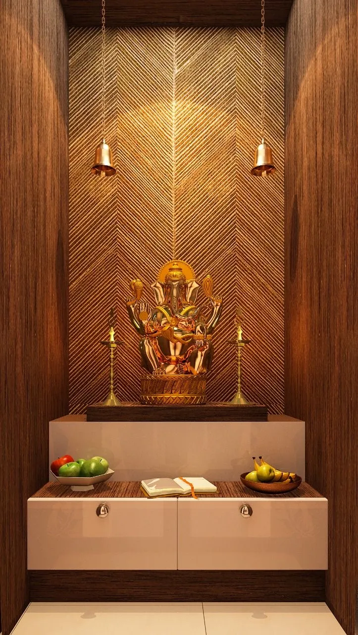 A pooja niche with a herringbone-textured gold wall panel behind a brass Ganesha idol, hanging temple bells
