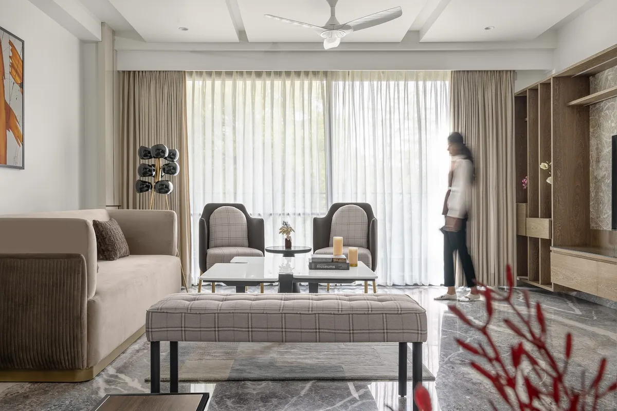 Living room with a beige velvet sofa facing two checked-wool tub chairs, a long tufted bench on black legs and paired white marble coffee tables