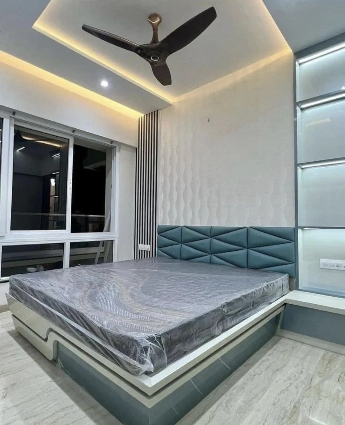 Master bedroom with a teal geometric-tufted headboard, a 3D wave-textured accent wall, a backlit frosted-glass wardrobe, and a cove-lit ceiling