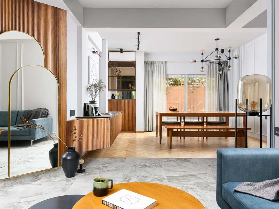 Open-plan living and dining zoned by a change from grey marble to herringbone oak, with a fluted teak wall and arched brass mirror at one end