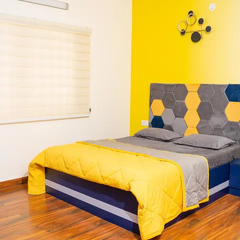 Bedroom with a navy bed frame, grey-and-yellow hexagon-tufted velvet headboard, and a yellow accent wall behind it.