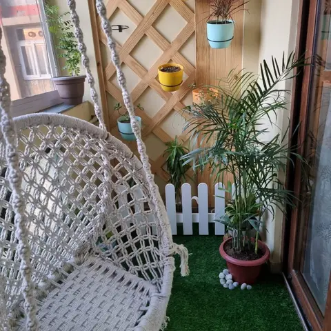 Balcony with a macrame hanging swing chair, artificial turf underfoot, and a wooden lattice trellis holding colourful