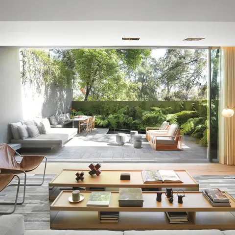 Living room with tan leather sling chairs, a two-tier wood coffee table styled with books and objects, and floor-to-ceiling