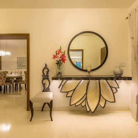 Entrance foyer with a sculptural gold lotus-petal console table beneath a round black-framed mirror, a carved baroque-style