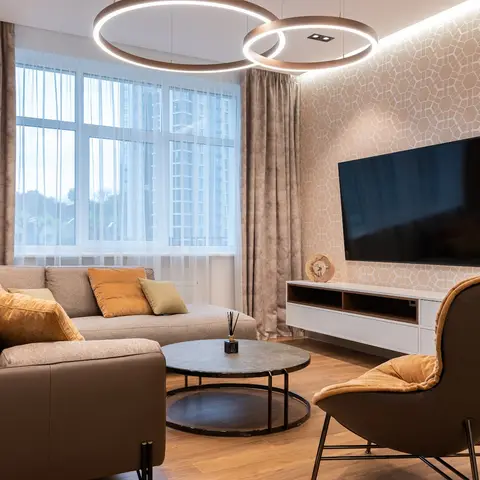 A living room with a geometric-patterned accent wall behind a floating TV console, twin ring pendant lights, and a brown