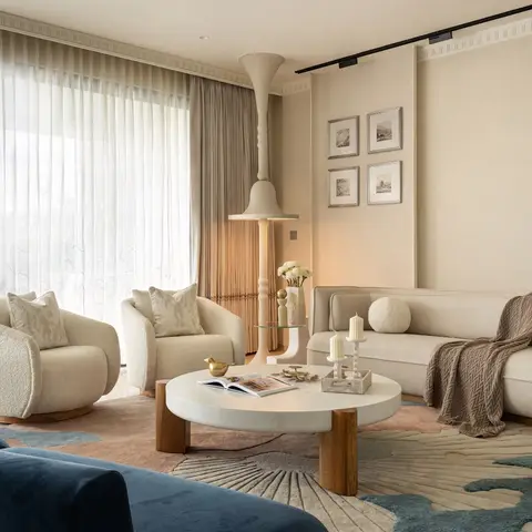 A living room with boucle swivel armchairs and a navy velvet sofa around a round marble-and-wood coffee table, sheer