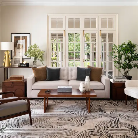 a bright living room with a cream tufted sofa, a wood-and-cane mid-century armchair, a bold black-and-white swirl-pattern