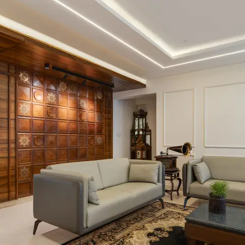 A carved wood feature wall in a brass-inlaid grid pattern anchors a living room with grey leather sofas, an antique display