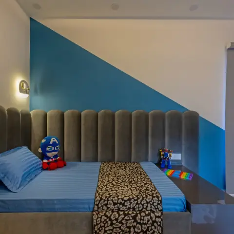 a boy's bedroom with a two-tone geometric blue and white painted wall behind a scalloped grey channel-tufted upholstered