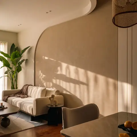 Sunlit open-plan space with a curved lime-plaster feature wall behind a beige sofa in the living zone and a marble dining