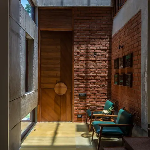 Home entrance with a diagonal-panel wood main door with a circular pull, an exposed brick wall, board-formed concrete, and