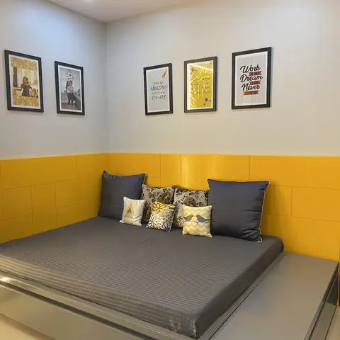 a girl's bedroom corner with a mustard-yellow upholstered wainscot wall behind a low platform bed, and a gallery wall of