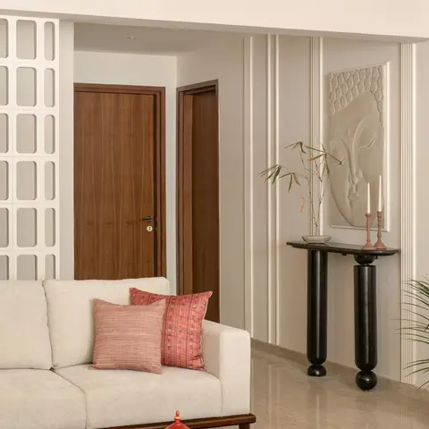 A living room corner with fluted plaster wall panelling, a carved stone Buddha-face wall relief above a black sculptural