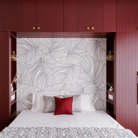 Bed nook framed by a fluted maroon wraparound wardrobe wall with brass handles, set against a monstera-leaf line-art
