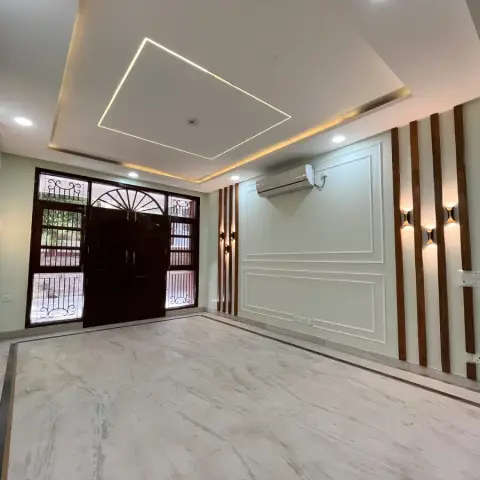 An empty entrance foyer with a diamond-shaped cove-lit ceiling, dark wood main door with wrought-iron grille glazing, fluted