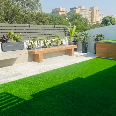 Rooftop terrace with artificial turf, a built-in stone bench and a floating teak bench, potted banana plants lined along a