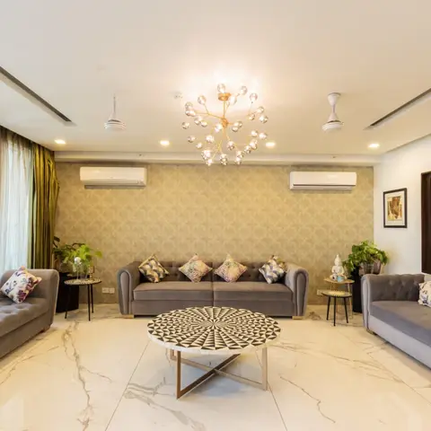 Living room with three tufted grey velvet sofas around a round mosaic-top coffee table, patterned gold-and-olive wallpaper