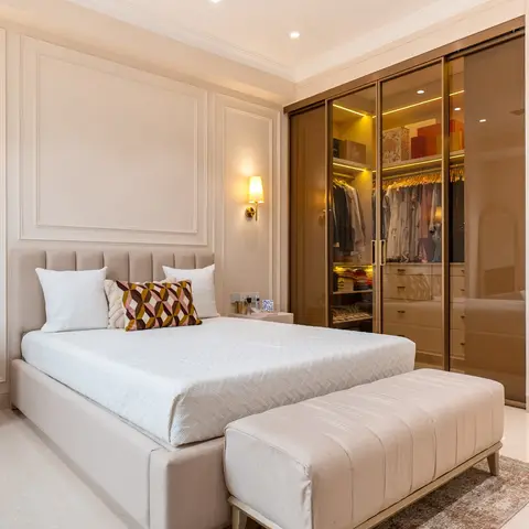 A cream panel-moulded master bedroom with a tufted upholstered headboard, brass wall sconces, an upholstered bench at the
