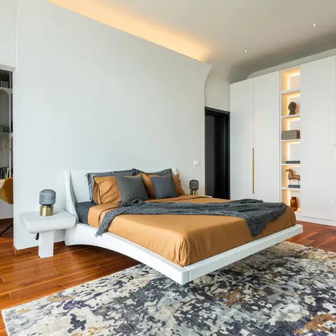 Bedroom with a floating cantilevered curved bed platform in white, rust-orange bedding, a curved cove-lit ceiling drop and a