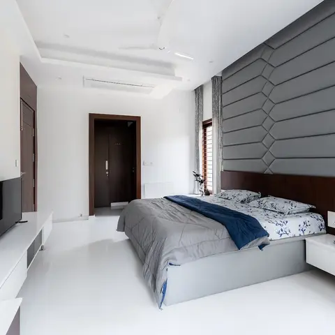 All-white minimalist bedroom with a grey chevron-channel upholstered headboard wall rising to the ceiling and a glossy white