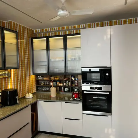 Modular kitchen with a bold orange-and-yellow plaid mosaic tile wall, ribbed glass upper cabinets with amber lighting, and a