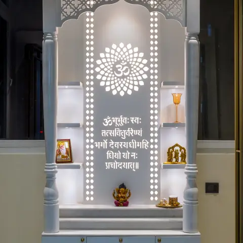A backlit pooja unit with a carved jaali arch, a Gayatri Mantra text panel, brass idol niches on either side and a marble
