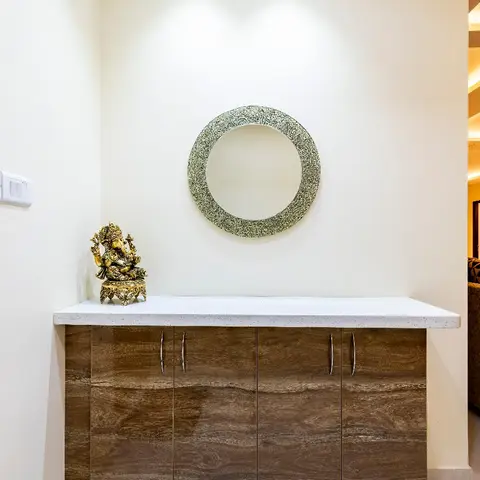 Entryway console in wood-grain high-gloss finish with a white stone top, a round textured mirror above, and a brass Ganesha