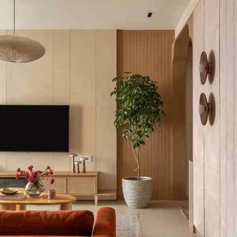 Living room with a rust-velvet sofa and round wood coffee table facing a cane-front TV console against a plaster-textured