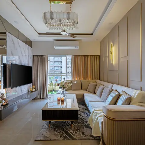 L-shaped beige living room with a mirrored-and-marble TV feature wall, brass wall sconces, a crystal chandelier over a