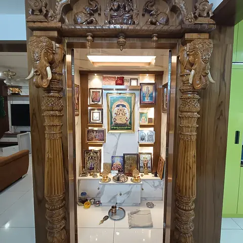 An elaborately hand-carved teak temple unit with twin elephant-head brackets and pillars framing a marble-backed shrine wall