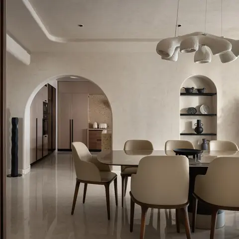 Dining area with a sculptural cream ceramic pendant light over an oval marble-top table with cream leather chairs, framed by