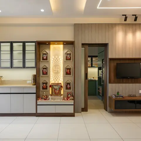 Open living space showing a backlit pooja niche with a lotus motif and deity frames, flanked by a glass-front crockery unit