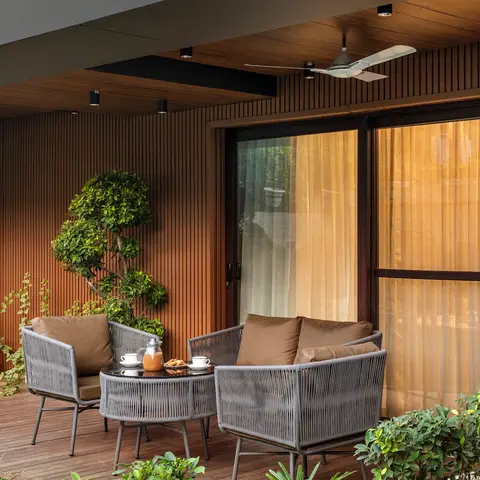 Covered balcony with vertical timber slat wall cladding, wood decking, and a grey woven-rope outdoor seating set around a
