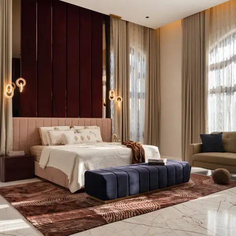 Master bedroom with a deep maroon channel-panelled wall behind a blush upholstered headboard, a navy channel-tufted bench at