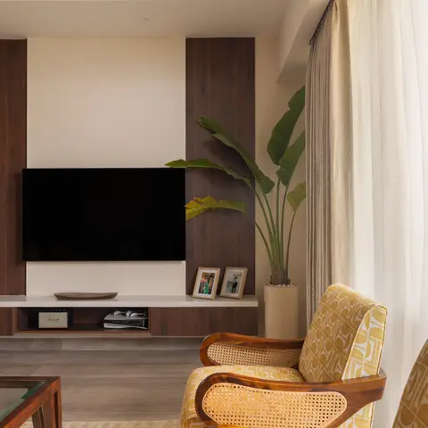 Living room with a walnut-panelled TV wall, cane-back mid-century armchairs in mustard print fabric, and sheer curtains by