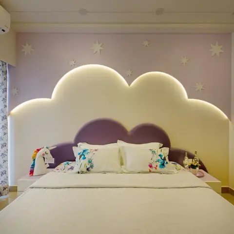 Child's bedroom with a cloud-profile headboard panel backlit in warm LED against a lilac wall scattered with white star