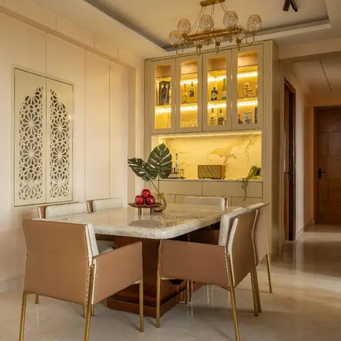 A dining room with a marble-top table on a brass-trimmed base, tan leather-and-cane chairs, and a backlit glass-front bar