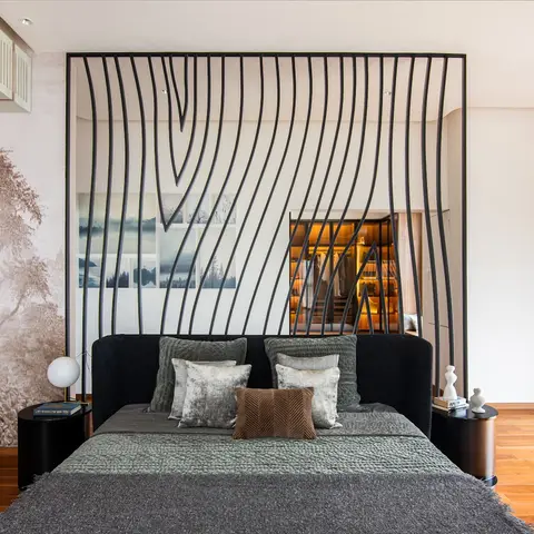 Master bedroom with a sculptural wave-patterned black metal headboard screen framing a glimpse of the attached walk-in