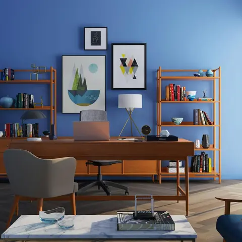 Home study with a bold blue accent wall, mid-century walnut desk and open bookshelves, a gallery of framed art, and a marble