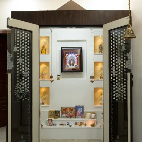 Freestanding pooja unit with etched glass-and-wood doors featuring om and swastik motifs, backlit niches for deity idols, a