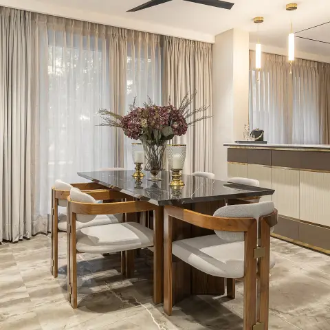 Walnut-framed dark-marble dining table for six with curved boucle armchairs, backed by full-height sheer and pinch-pleat