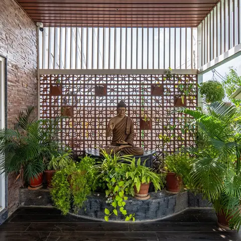 Home balcony garden corner with a meditating Buddha statue set against a jaali screen wall, densely arranged potted ferns